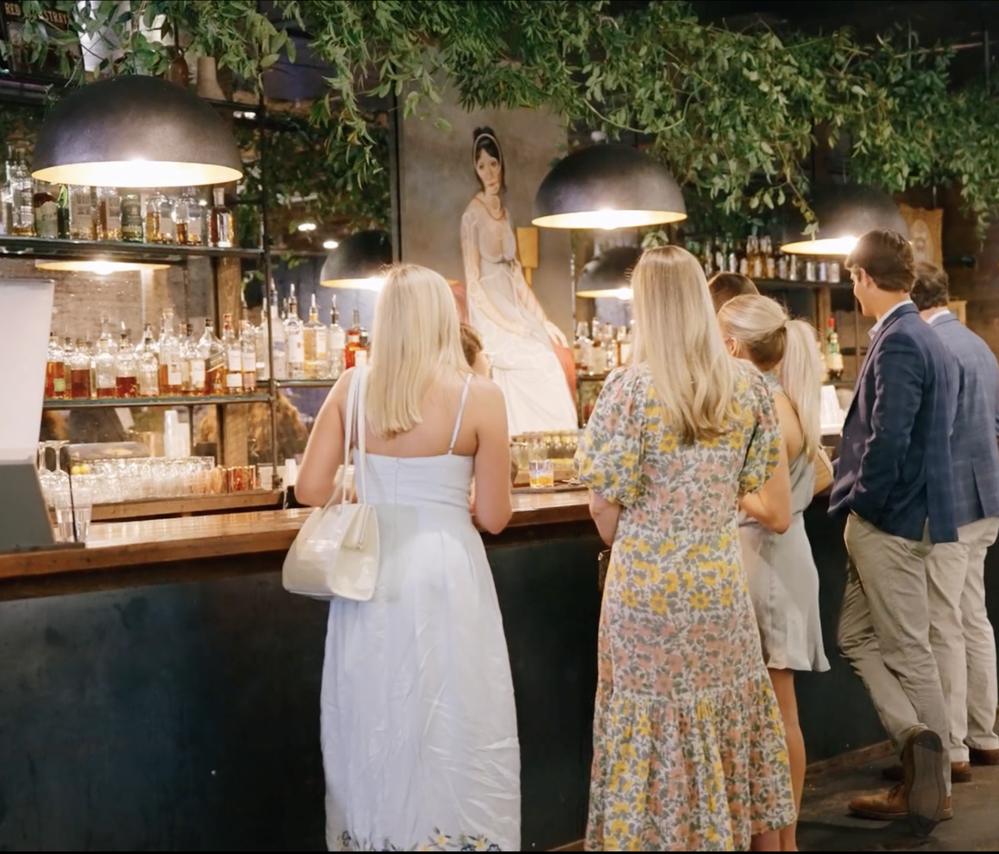 Guests at cocktail bar with hanging greenery, pendant lights and portrait painting