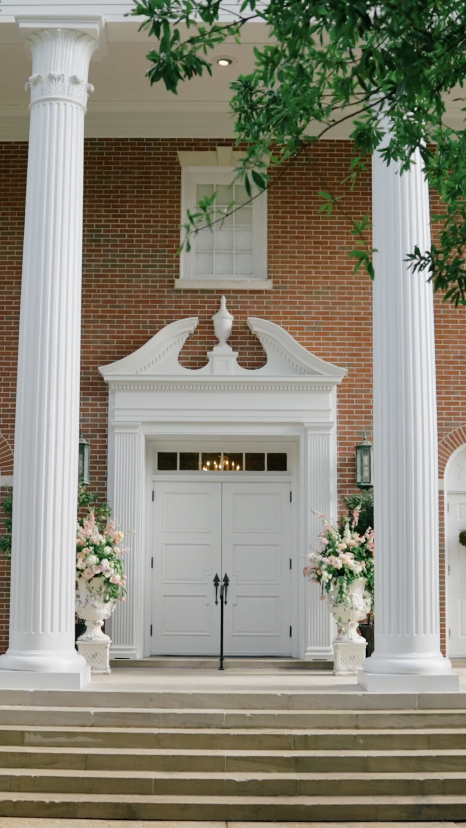 Colonial brick entrance with Corinthian columns and floral urns flanking white double doors