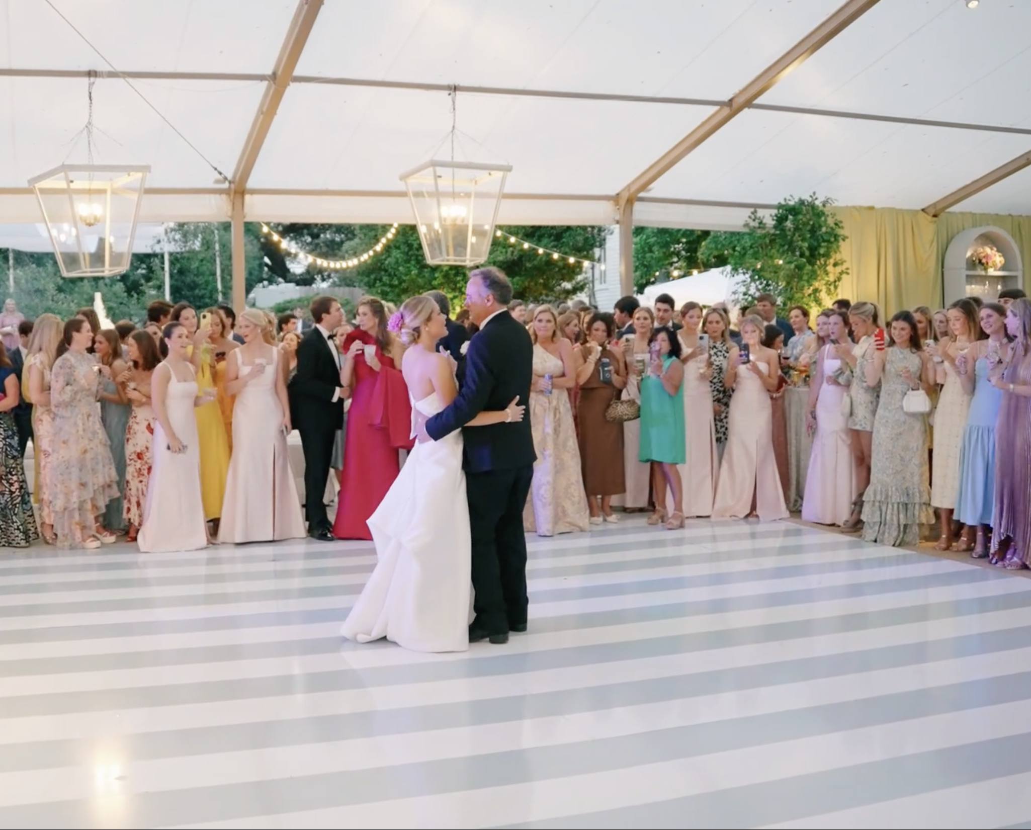 Bride and father first dance on striped floor under clear tent with lantern chandeliers