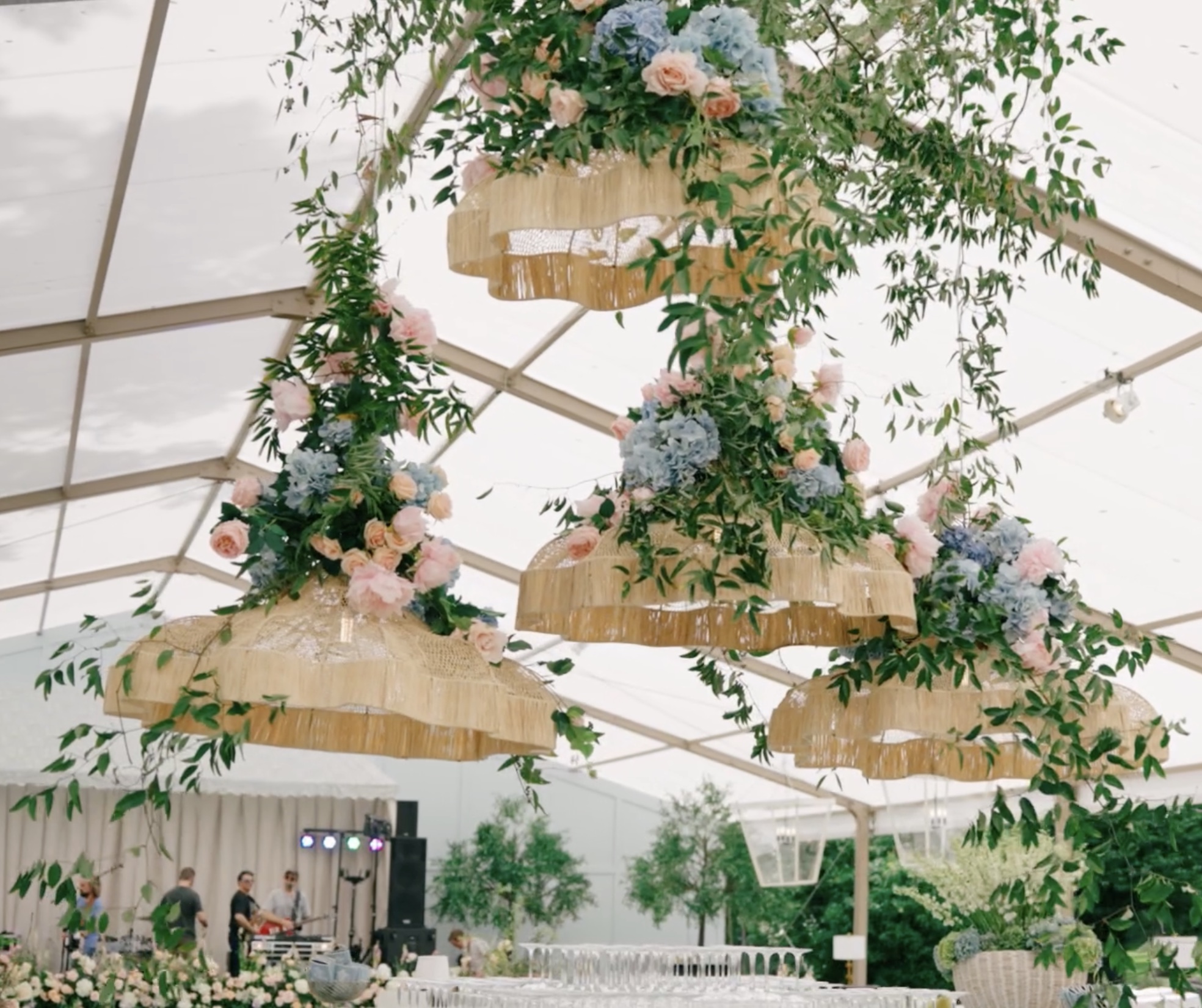 Floral-lined pathway with string lights leading to illuminated reception tent at dusk