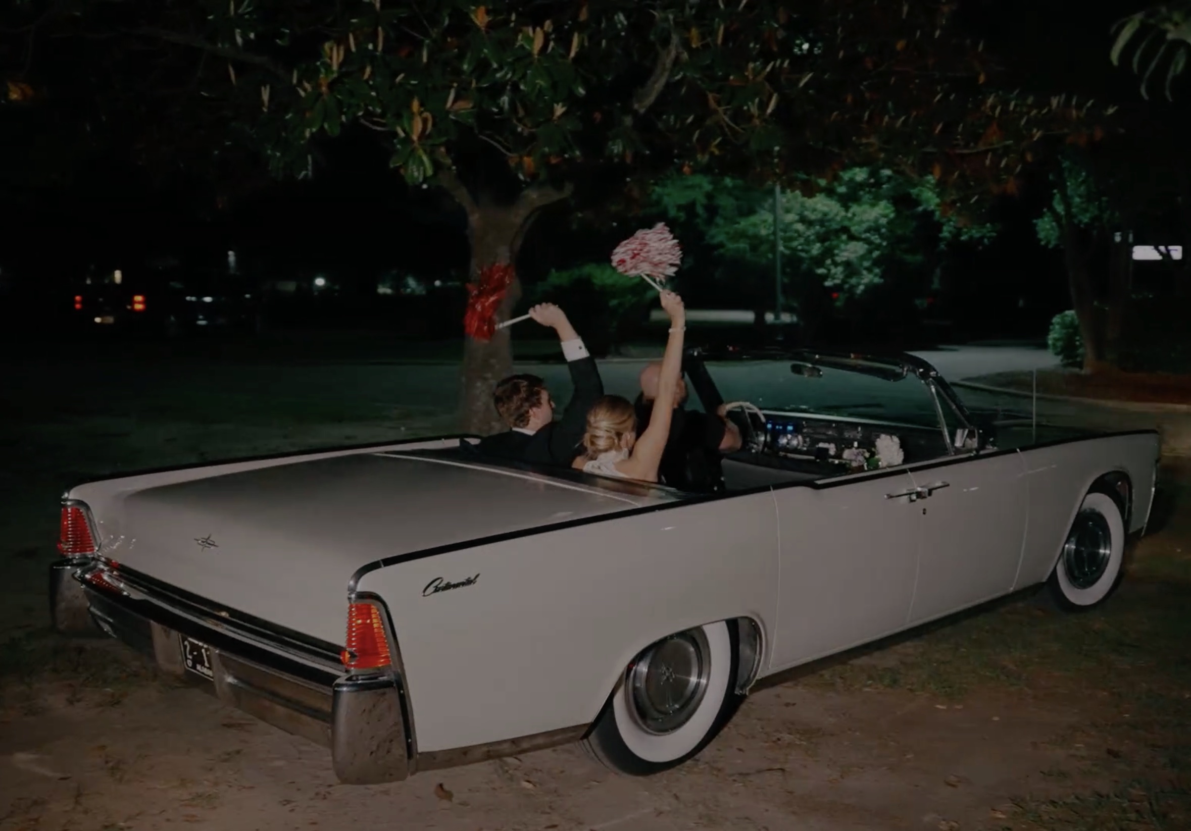 Bride and groom in vintage Lincoln Continental convertible getaway car at night